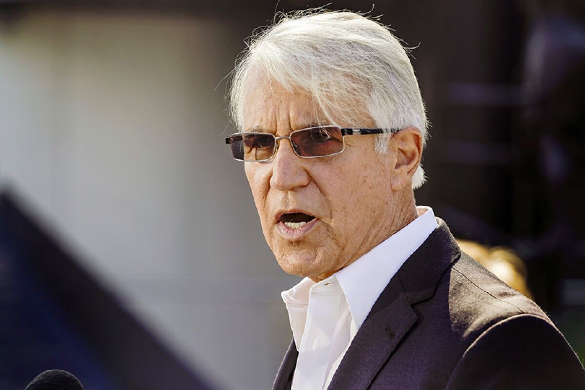 A white-haired man in sunglasses, a white shirt and a dark blazer.
