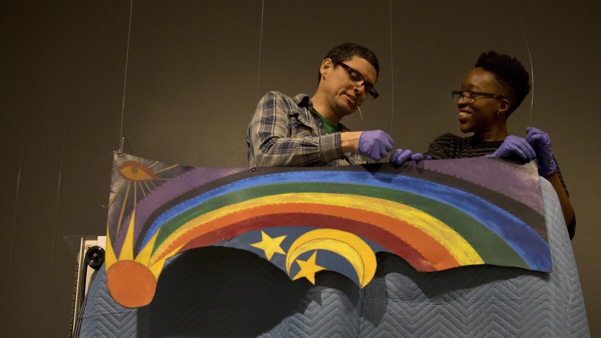 Preparator Arturo Guzman, left, and Nya Abudu, assistant preparator, install "Rainbow Mojo," 1972, acrylic painting on cut leather by Betye Saar.