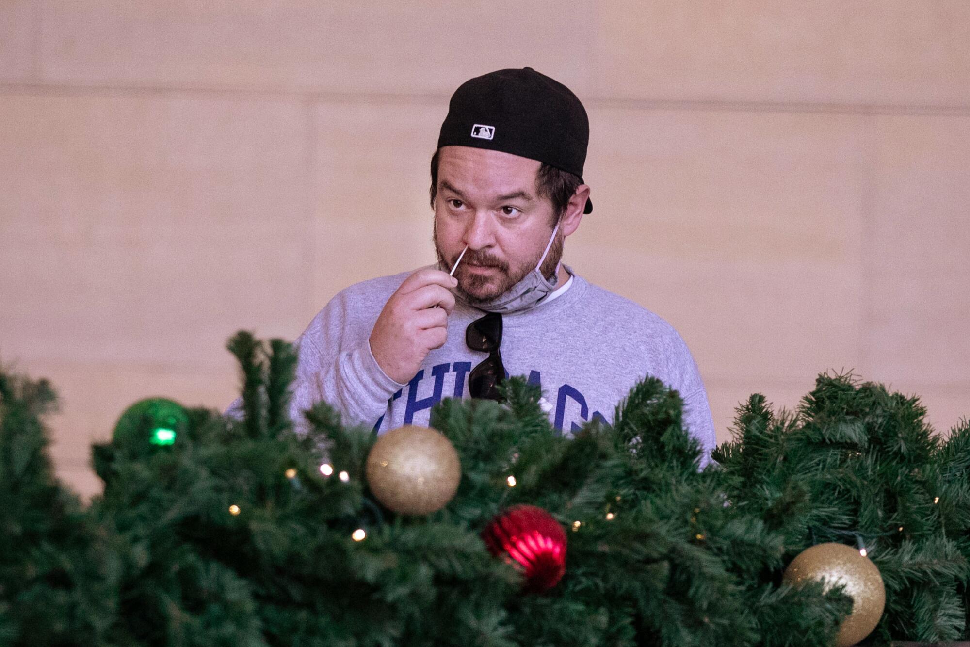A man swabs his nose near Christmas decorations.