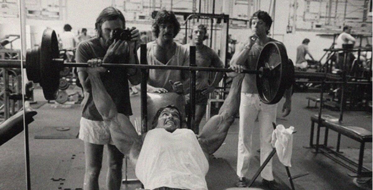 George Butler holds a camera as Arnold Schwarzenegger bench presses at a Venice gym in 1976.