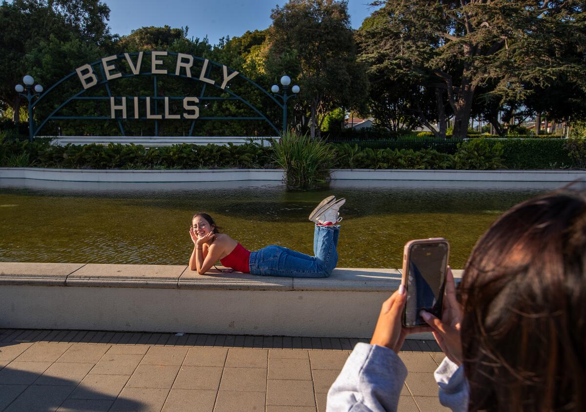 One person poses in front of a Beverly Hills sign while another person takes their photo