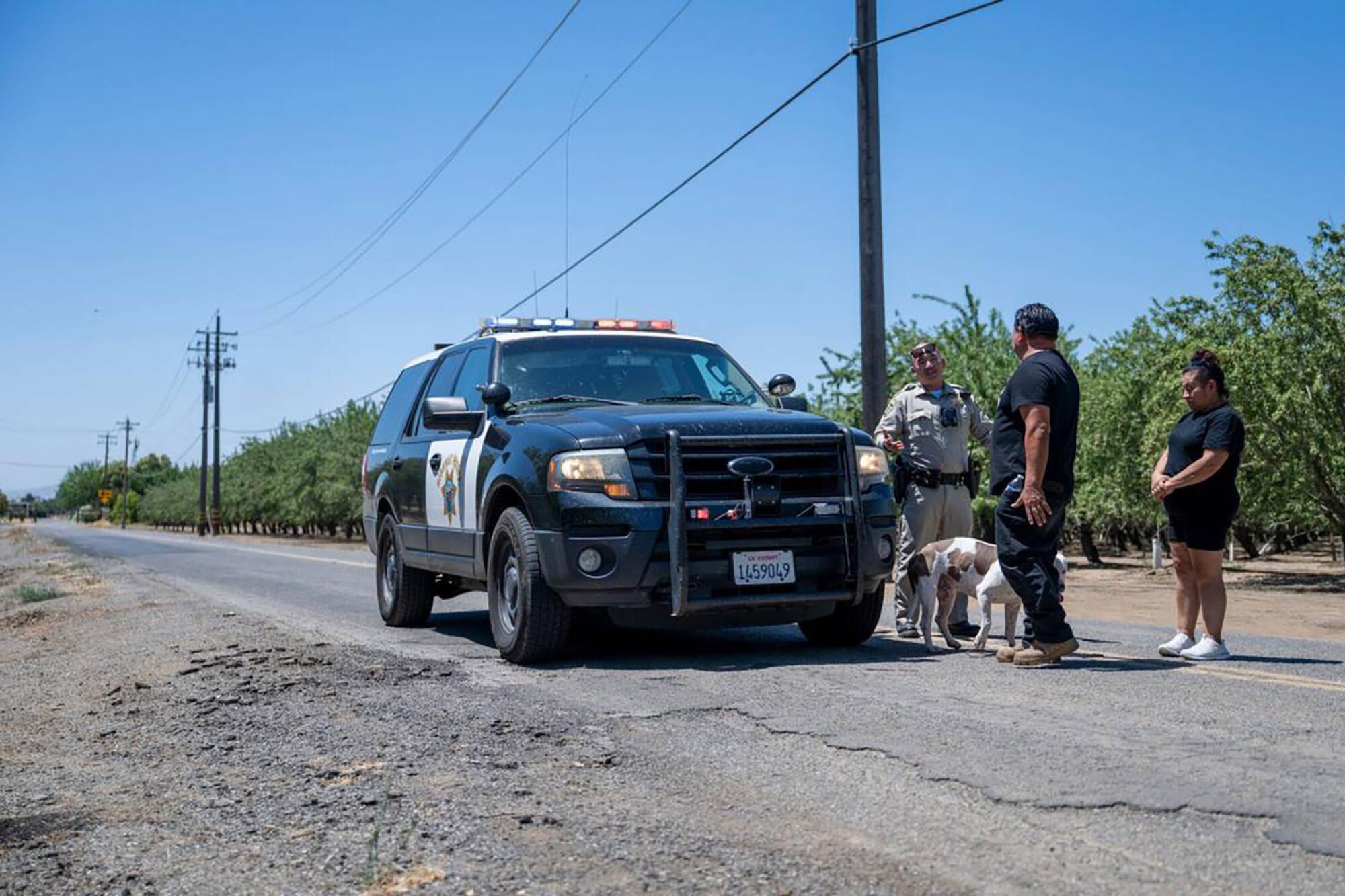 Two people speak with a Highway Patrol officer next to his vehicle.