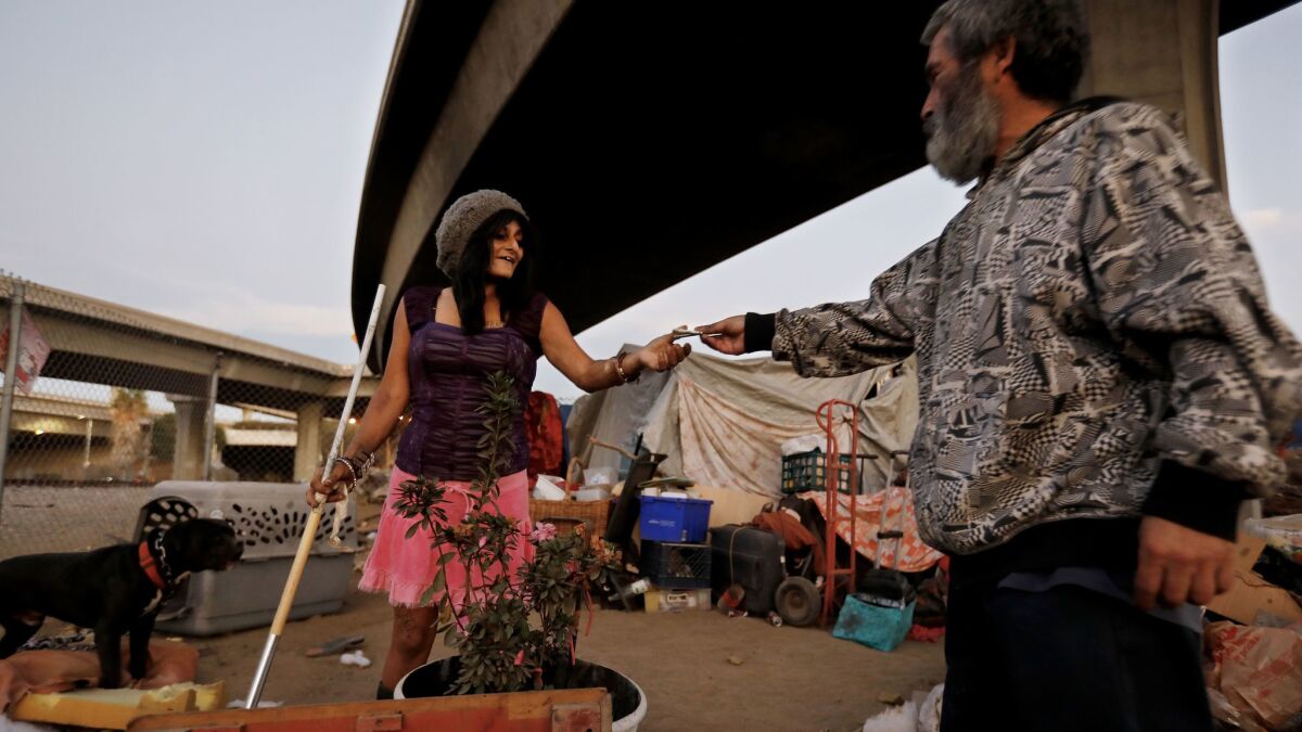 Samantha Sandoval, 40, left, is given a dollar by Margarito Alvarez, 56, her neighbor, at her tent where she has lived for a year at a homeless camp along West 117th Street and South Broadway in Los Angeles.