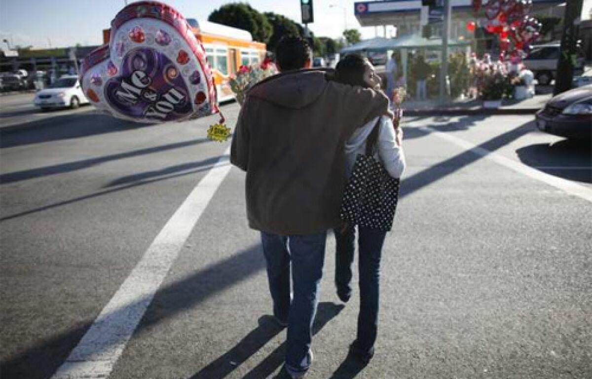 LOVE IS IN THE AIR: A couple strolls across 4th Street in Boyle Heights with Valentines Day gifts bought from street vendors. Sellers, carrying perfumes, teddy bears, underwear and balloons, set up shop at the corner of 4th and Soto Street.