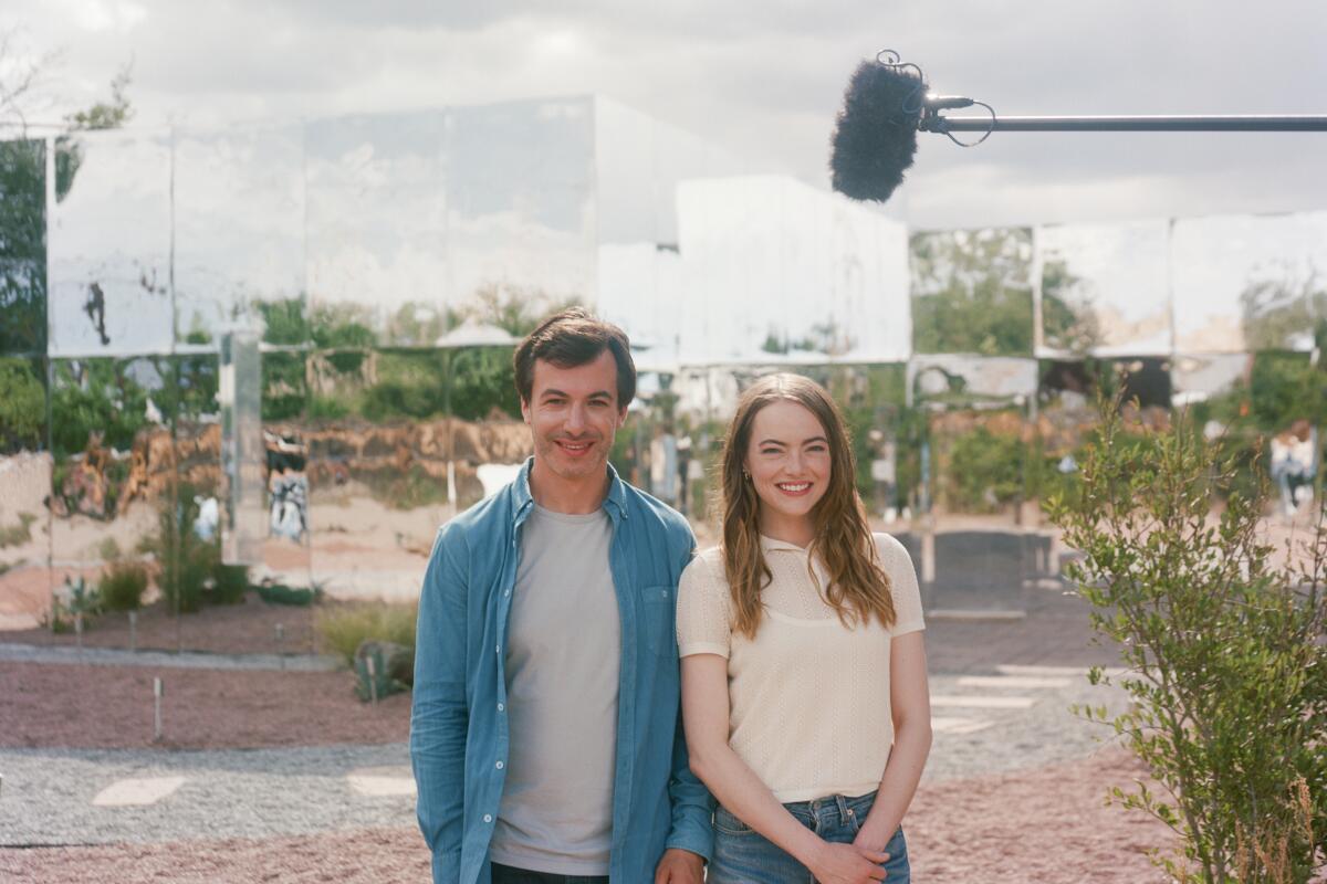 Asher and Whitney stand in front of a house covered in mirrors. A boom mic is reflected above them.