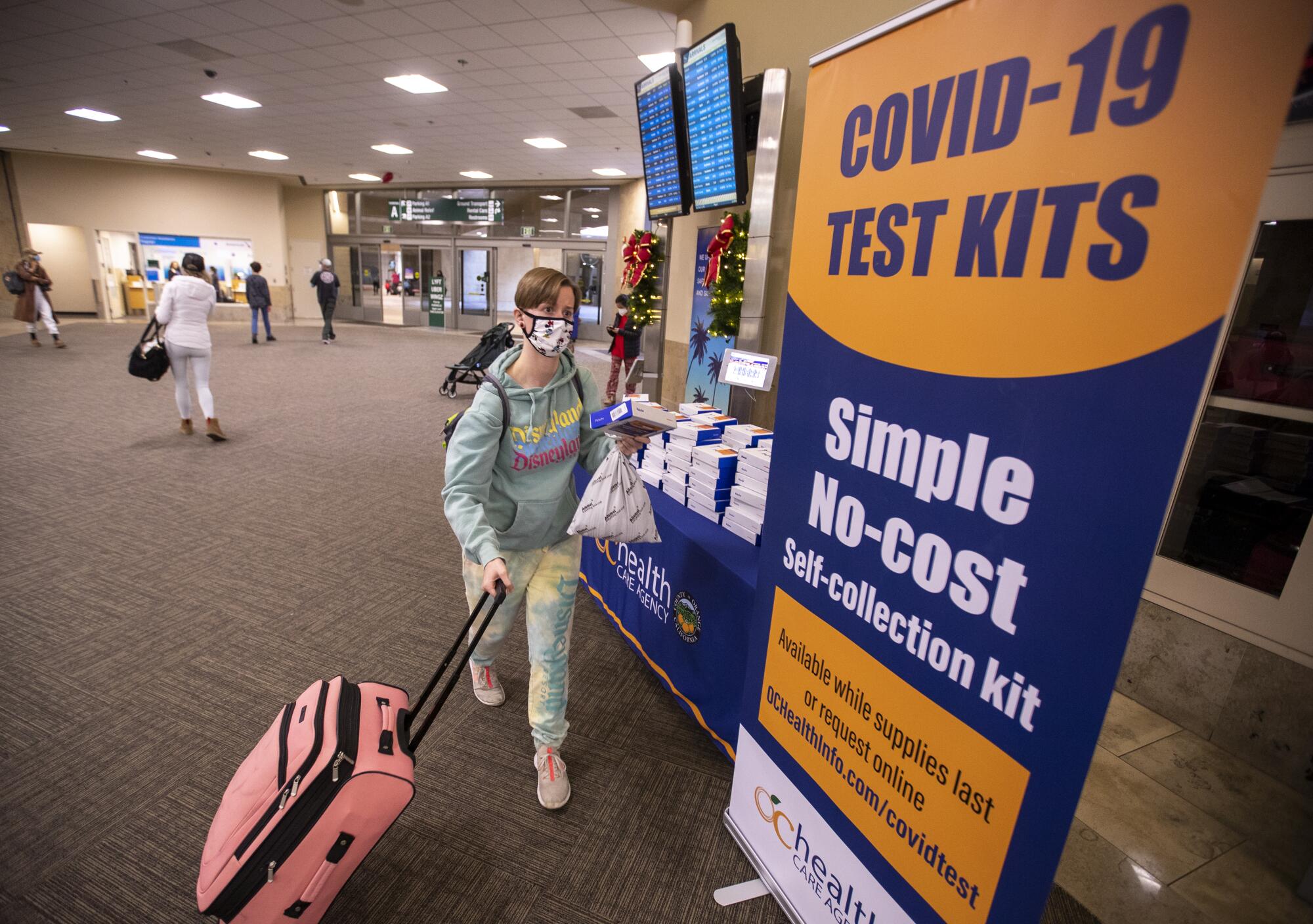 A woman with luggage picks up a COVID-19 test self-collection kit at John Wayne Airport
