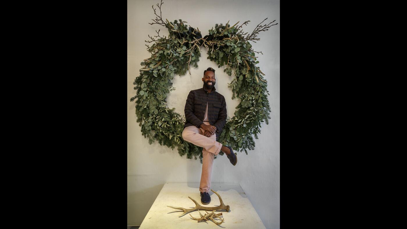 Maurice Harris, the proprietor of Bloom & Plume, posing with a wreath called "Raynesha Deer." Note: The deer antlers are made out of plastic.