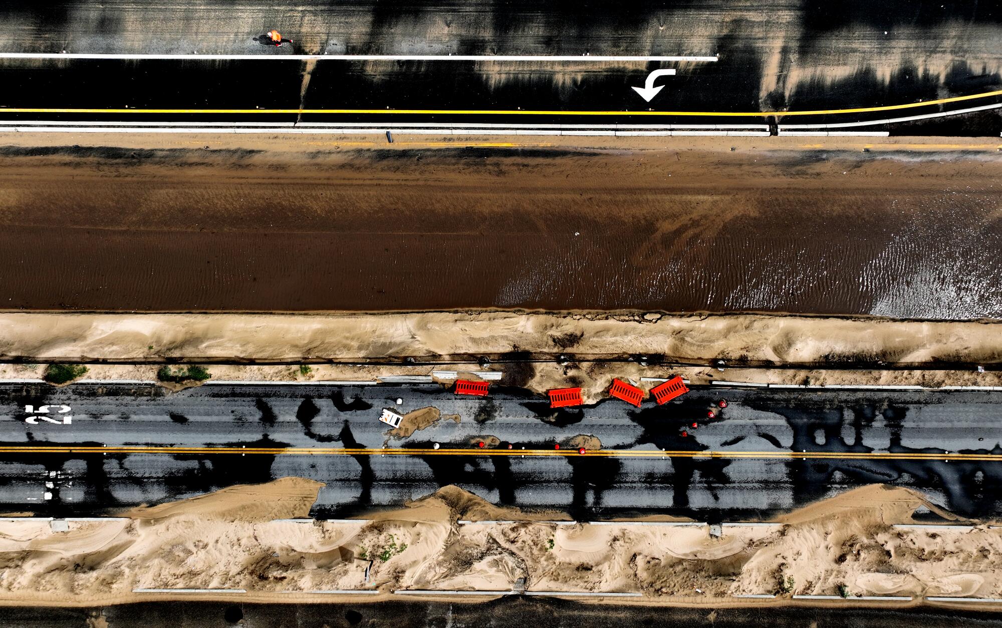 An aerial view of both lines of a highway, flooded with muddy and sandy water.