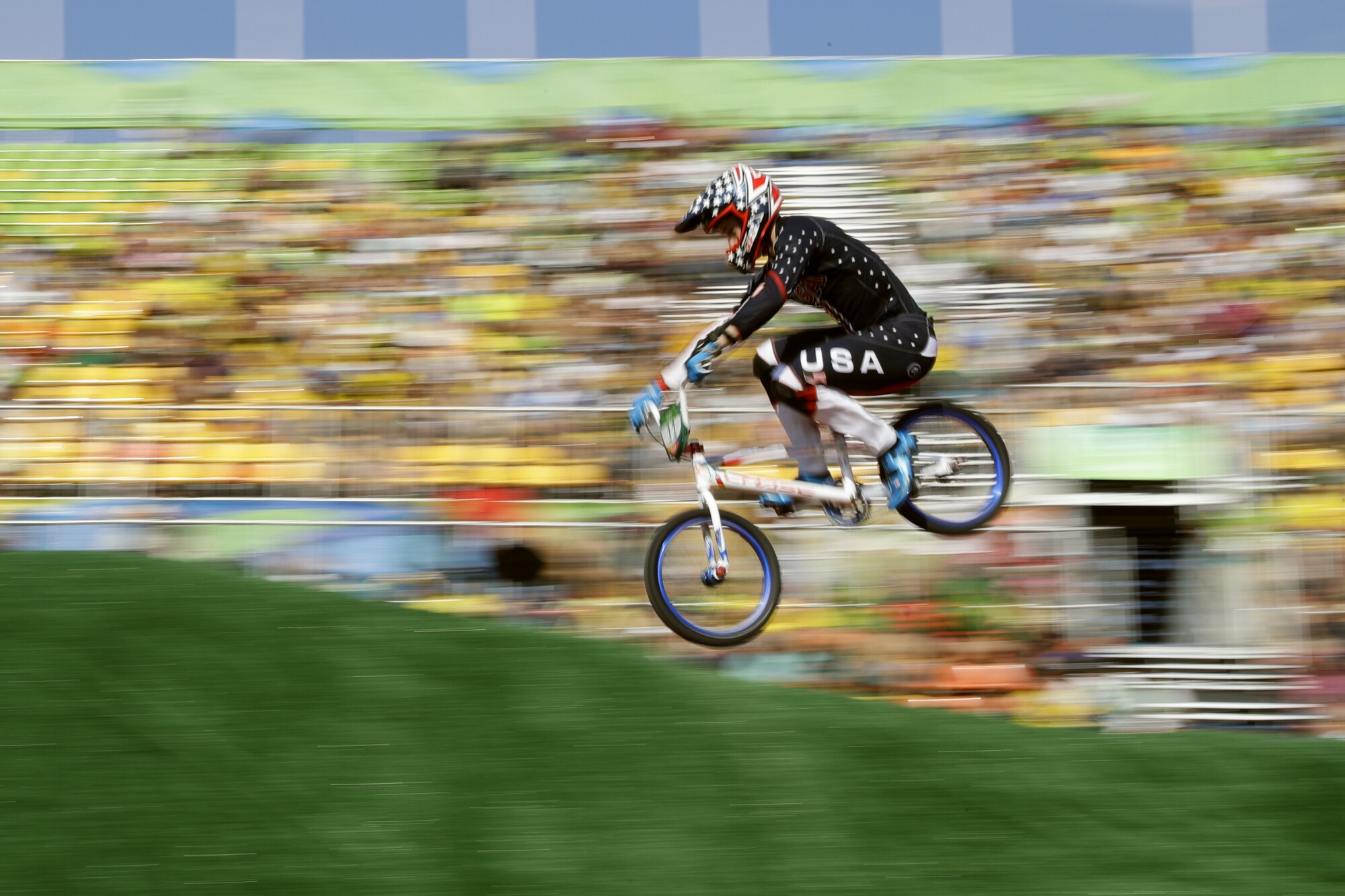 A BMX rider flies against a blurred backdrop of seating stands. 