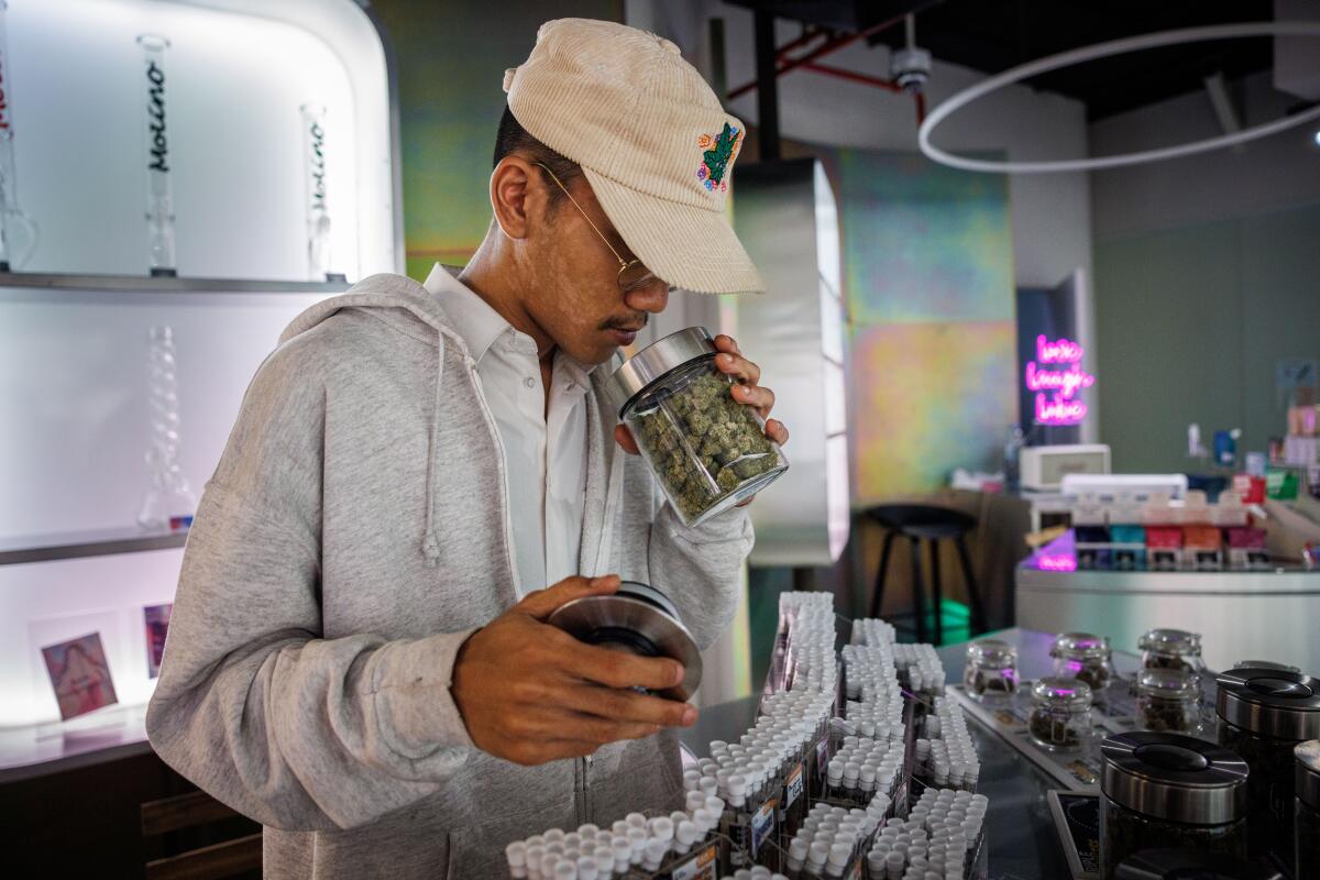 A man in a white cap and white jacket holds a glass dispensary jar to his nose 