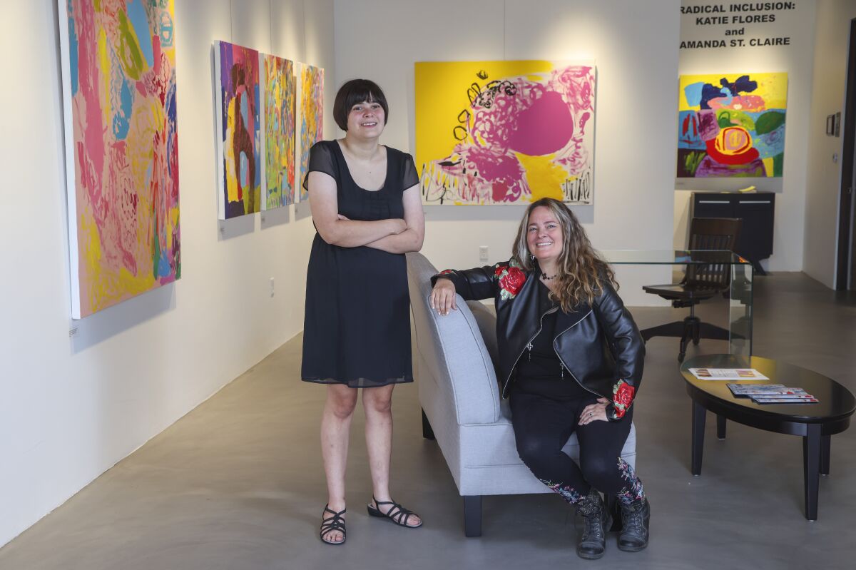 Painters Amanda Saint Claire (right) and Katie Flores pose for photos with their collaborations at an art gallery