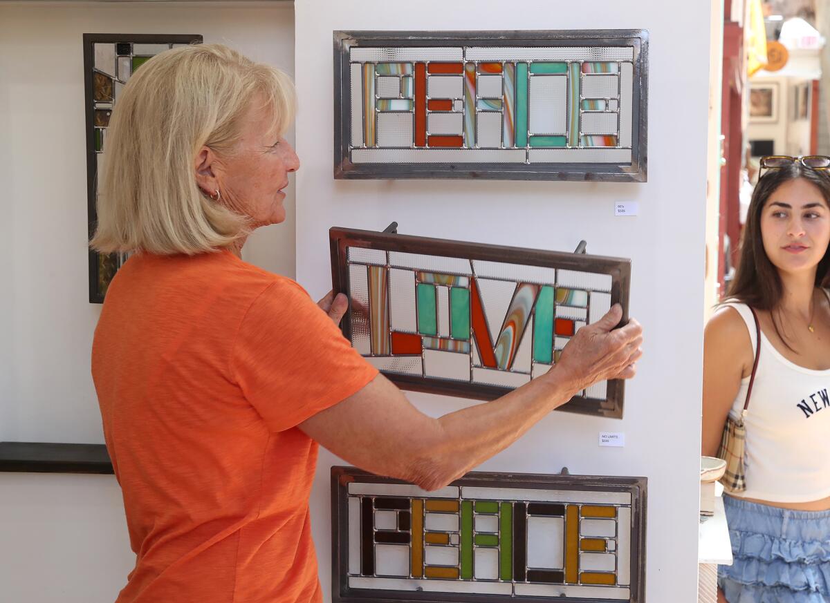 Stained-glass artist Barbara Bond hangs her work in her booth at the Sawdust Art Festival in Laguna Beach.
