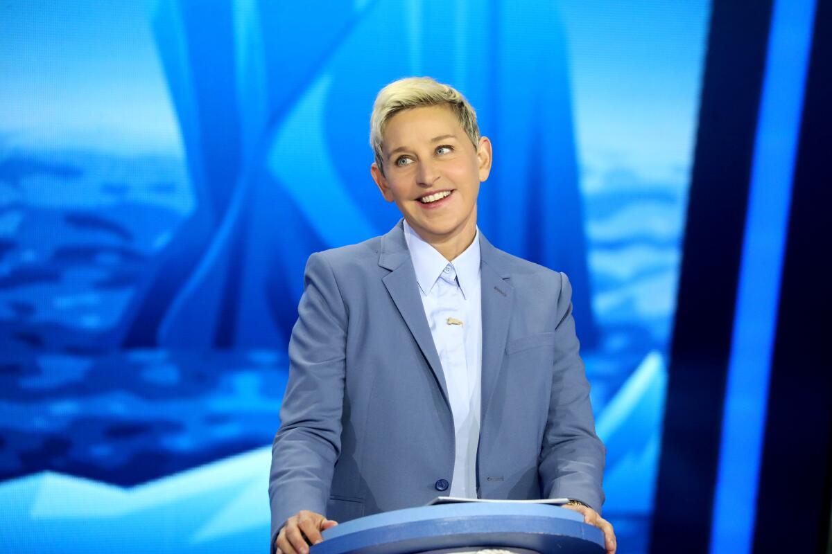 Ellen DeGeneres wearing a gray suit against a blue background