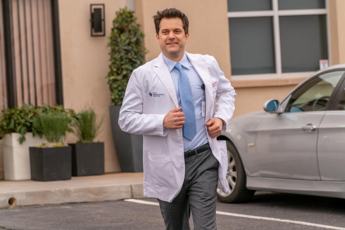 A man in a shirt, tie and white lab coat jogging and smiling