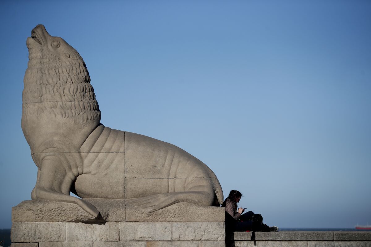 A woman sits next to a statue of a sea lion on the waterfront on Oct. 10 in Mar del Plata, Argentina.