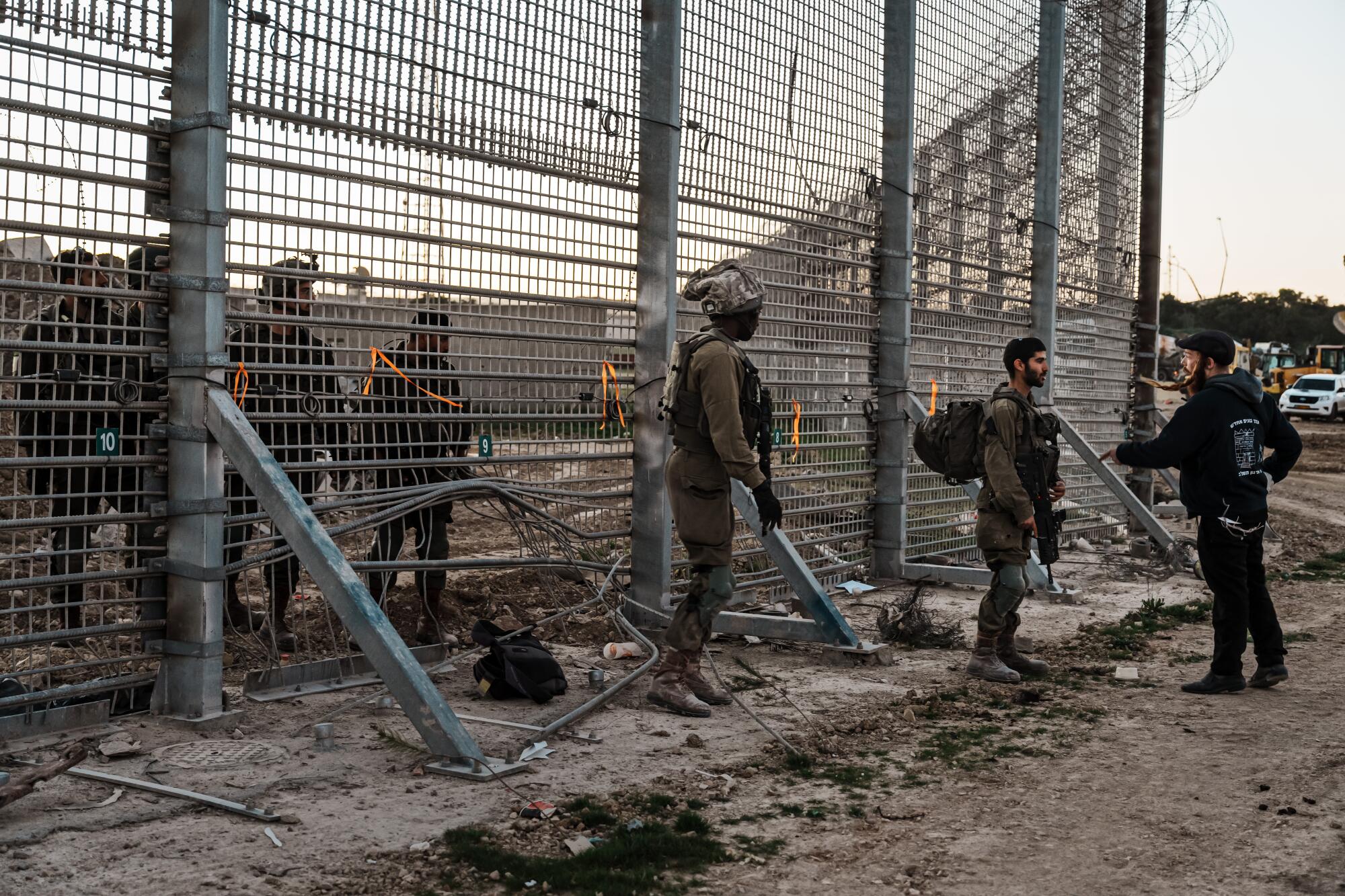 A soldier faces down one man as he approaches a tall security fence with troops on both sides