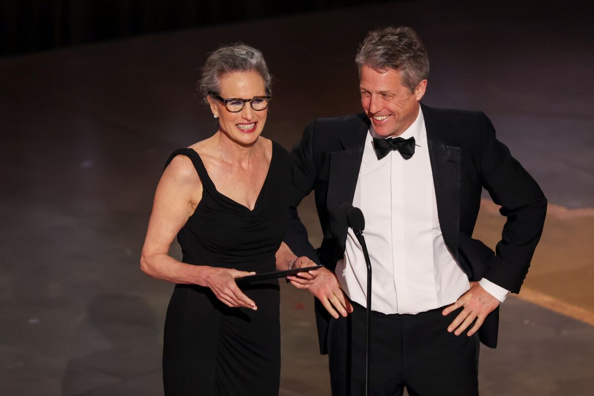 A woman in a black gown and a man in a tuxedo stand behind a microphone