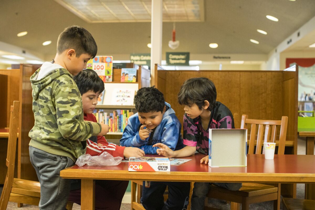 Four boys piece together a puzzle at a library table.