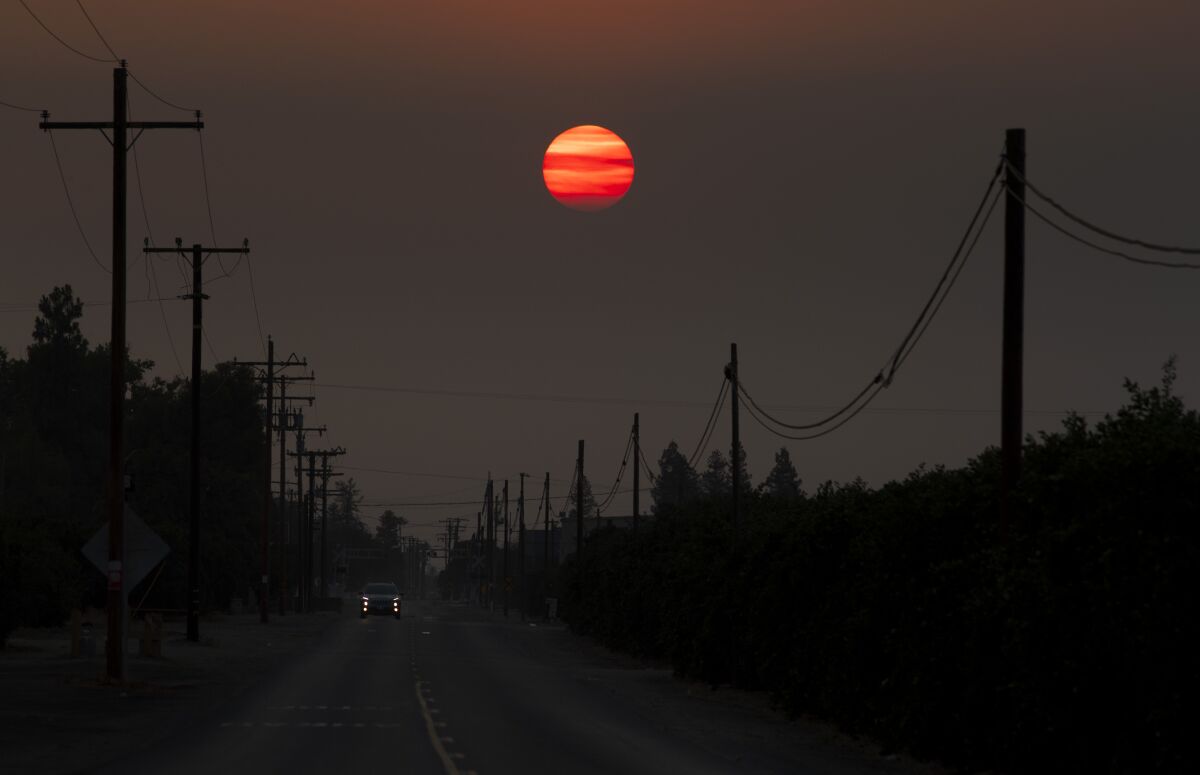 An orange setting sun shrouded by thick smoke above a two-lane road