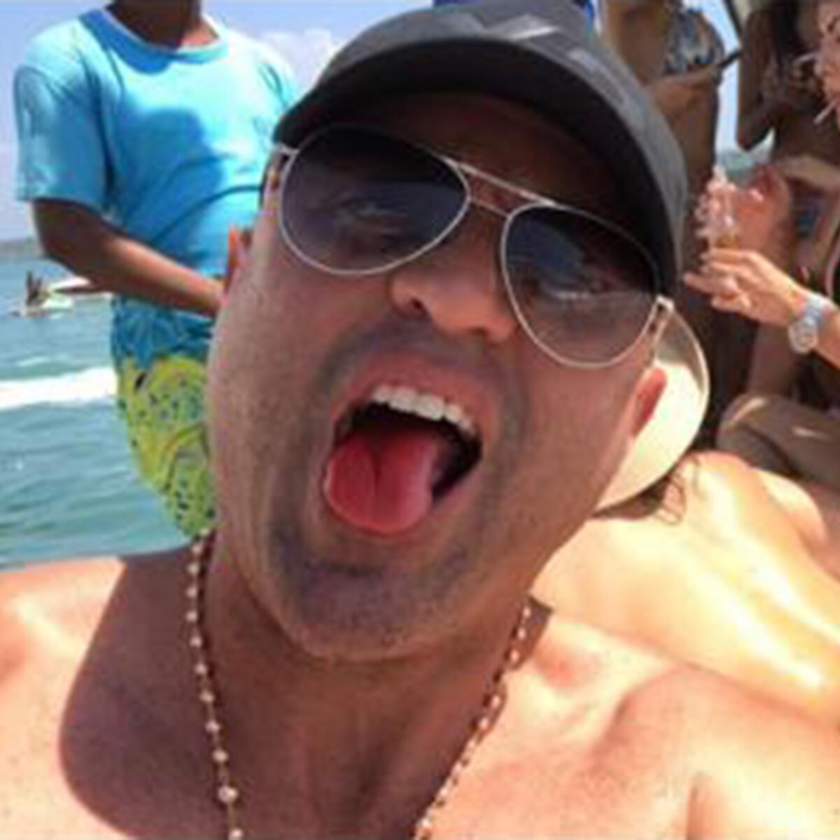 A man wearing sunglasses sticks his tongue out at the camera.