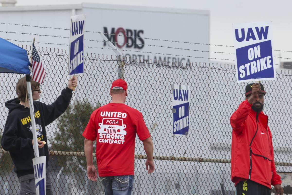 Pickets in red shirts strike outside a huge white factory building