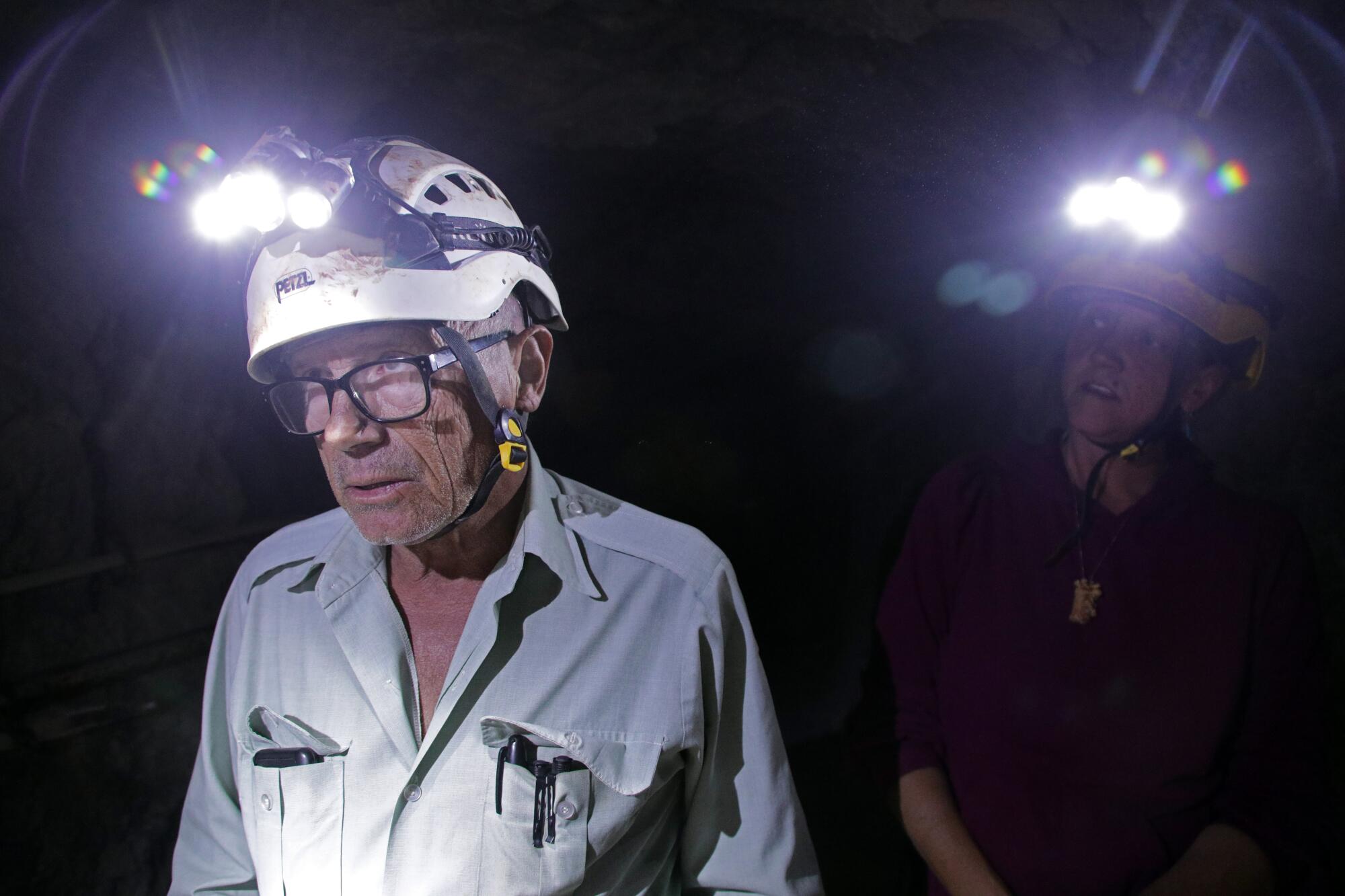 a man and woman wearing head lamps are underground in a dark cave.