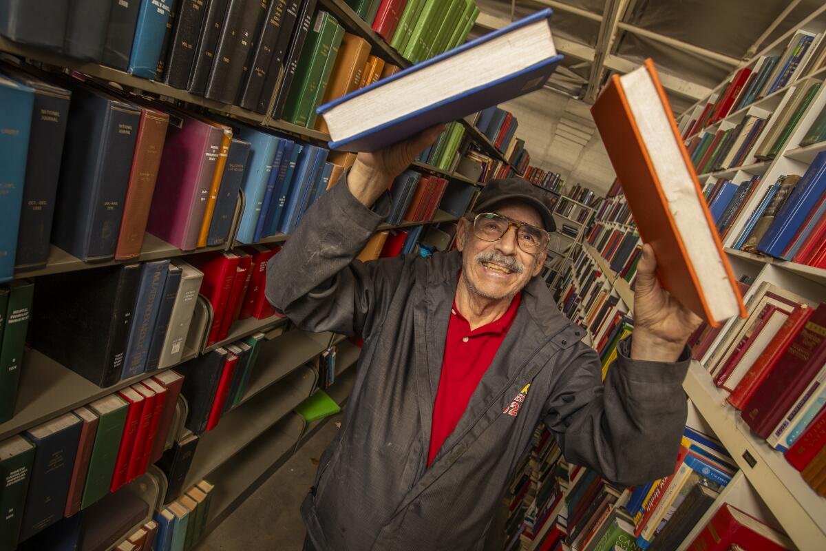 A man smiles and holds two large books over his head.