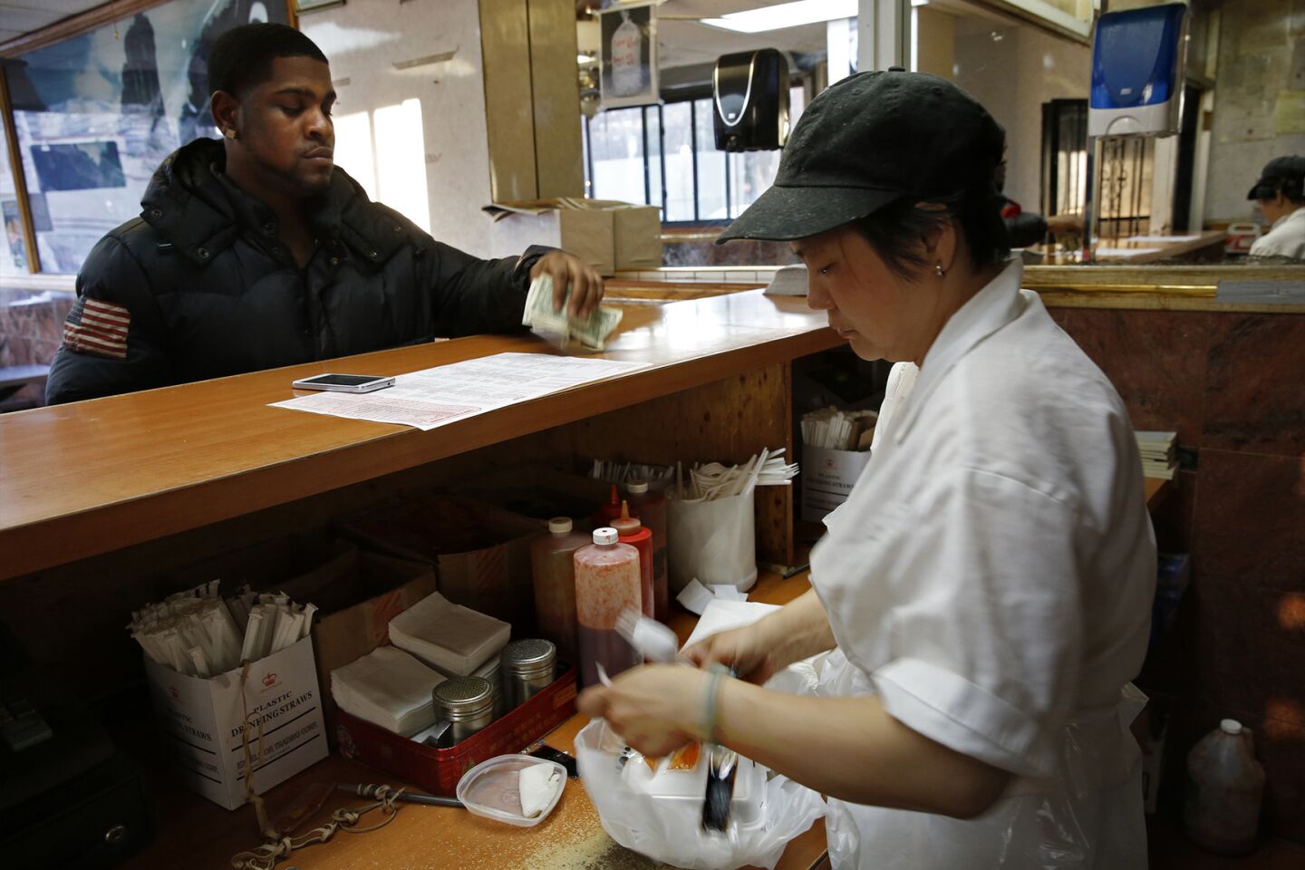 A cashier at China Doll Chinese Restaurant in Brooklyn, near the Pink Houses, gives change back to a customer.