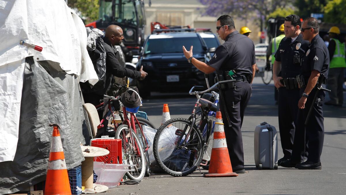 LAPD officers speaks with a man who is living in an encampment area in Los Angeles. Sanitation workers later cleaned the area. (Christian K. Lee / Los Angeles Times)