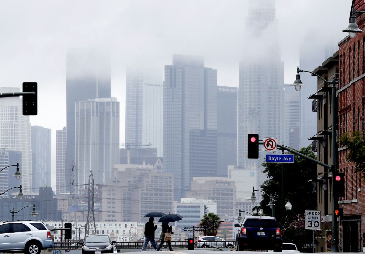 Pedestrians cross First Street in Boyle Heights as clouds partially obscure the downtown L.A. skyline on March 6. The first rain of fall made for a drizzly morning Sept. 26 in Los Angeles.