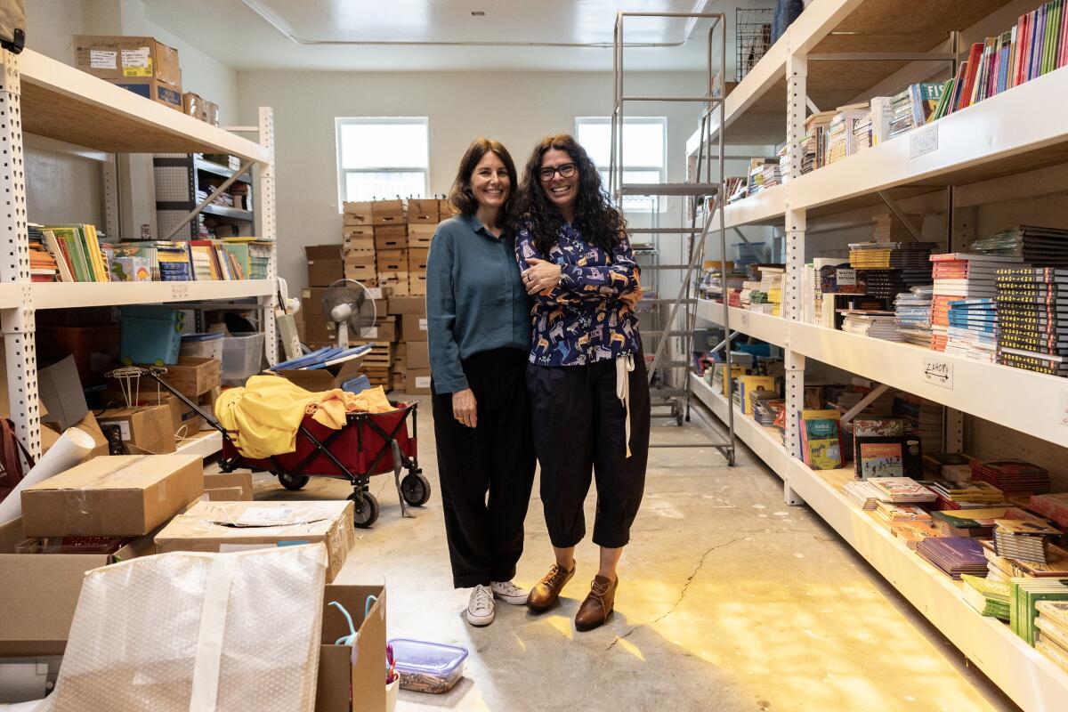 Two women stand between large shelves of books.