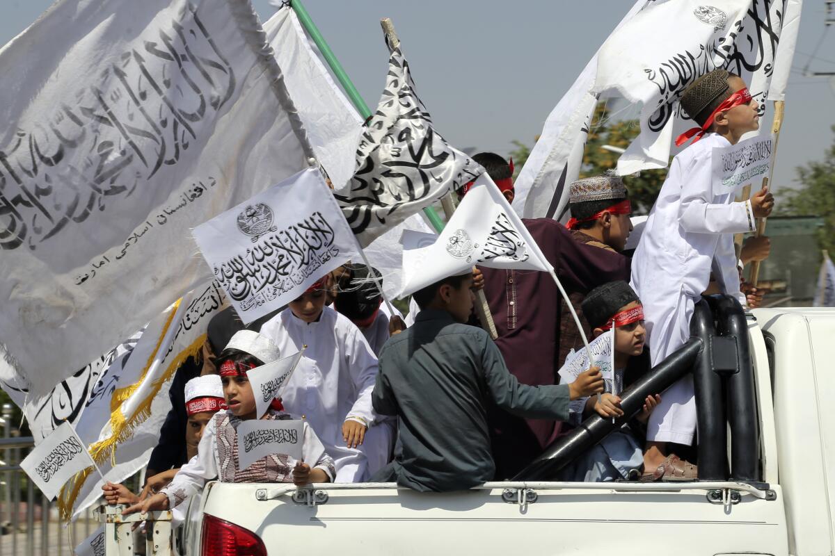 Children holding Taliban flags in the back of a pickup 