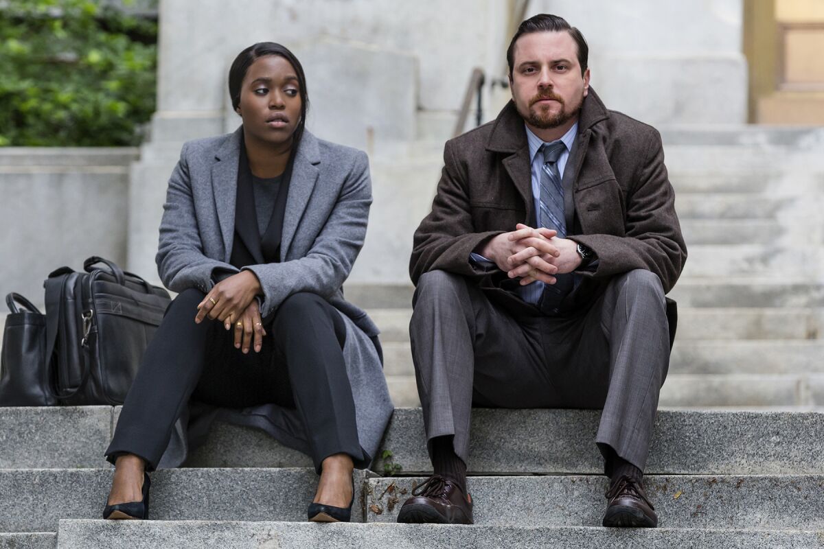 A woman and a man, both wearing suits, sit on some steps.