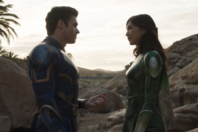 A man in a blue superhero suit facing a woman in a green superhero suit