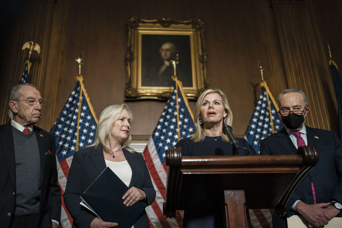Gretchen Carlson speaks at a lectern, joined by Senators Charles E. Grassley, Kirsten Gillibrand and Charles E. Schumer