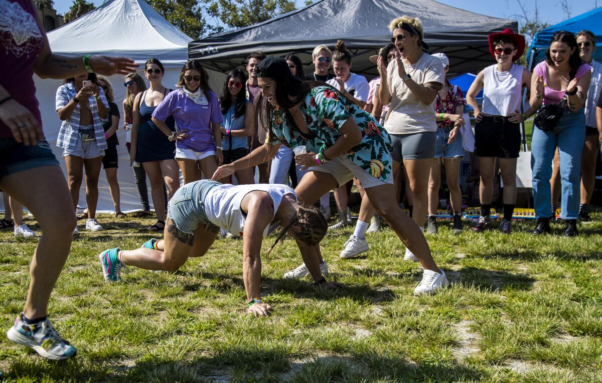 A person on all fours in a grassy field surrounded by others smiling and clapping