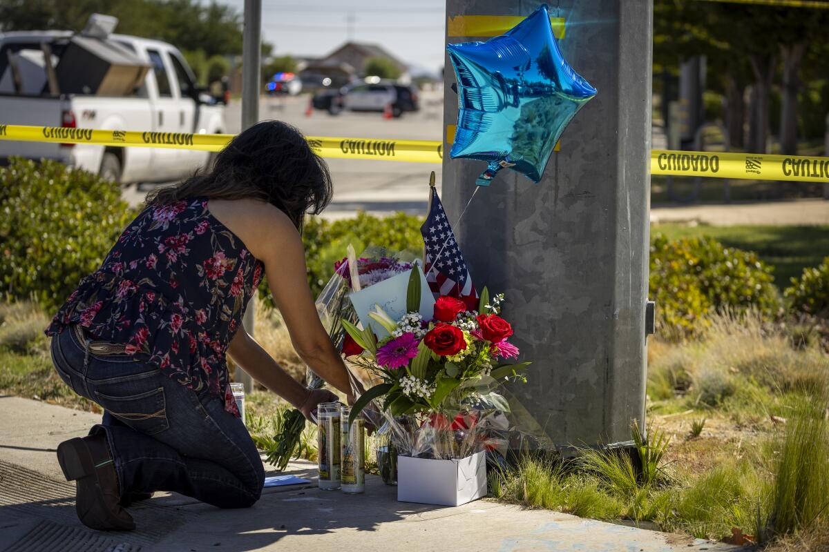 A woman places a candle, card and balloon at a growing memorial for Deputy Ryan Clinkunbroomer.