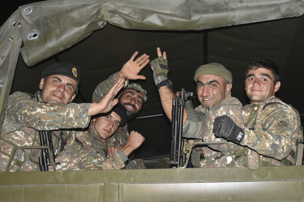 In this photo released on Tuesday, Oct. 6, 2020, Armenian soldiers wave to a photographer as they sit in a truck during fighting with Azerbaijan's forces in self-proclaimed Republic of Nagorno-Karabakh, Azerbaijan, Sunday, Oct. 4, 2020. The clashes have continued despite numerous international calls for a cease-fire. (Press office of Armenian Defense Ministry PAN Photo via AP)