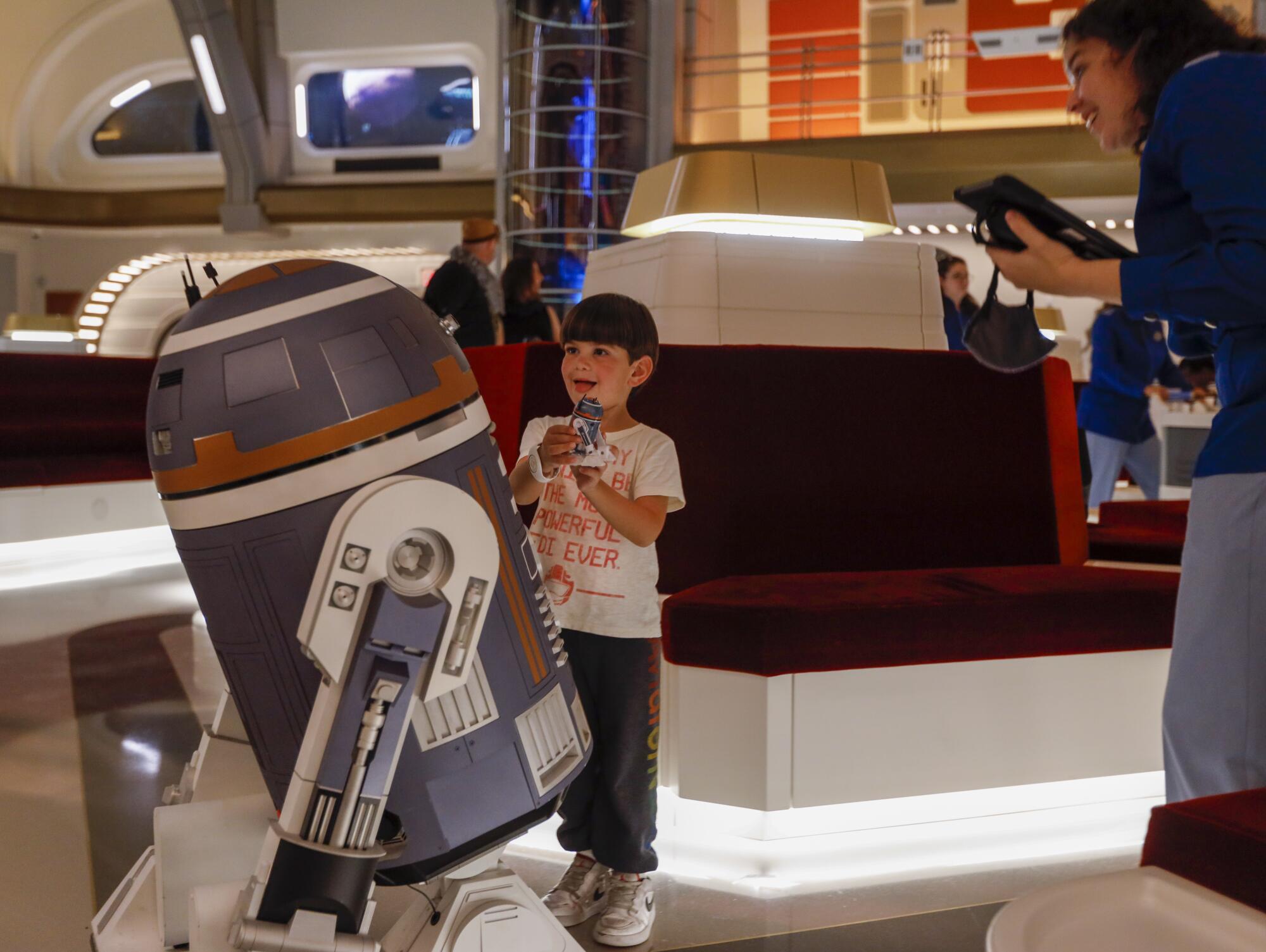 A young passenger, Joe, 5, shows his toy droid to SK-62O, an astromech droid.