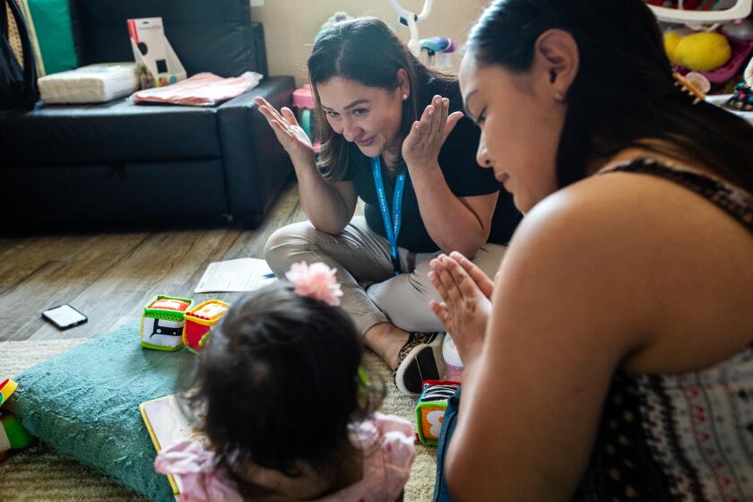 Compton, CA - August 23: Parent coach Alba Mariscal, middle, visits mother Ilse Ochoa, right, and ten-month-old baby Brianna de Leon, left, on Wednesday, Aug. 23, 2023, in Compton, CA. Parent coaches go house to house, checking in on these families through the first year of their baby's life. They offer tips and advice, and often just support in what is often a very challenging (though exciting) moment for new parents. But funding for this crucial program is at risk. First 5 is funded through a tobacco tax, and as more and more Californians give up their cigarettes, that funding money is starting to dry up. (Francine Orr / Los Angeles Times)