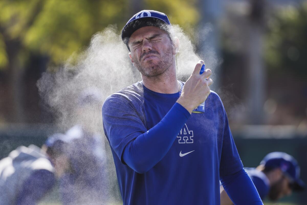 A baseball player sprays sunscreen on his face. 