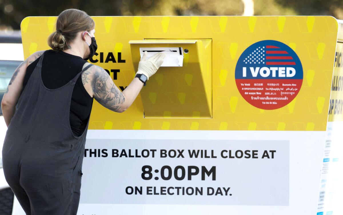 A woman drops off her ballot at a large yellow drop box.