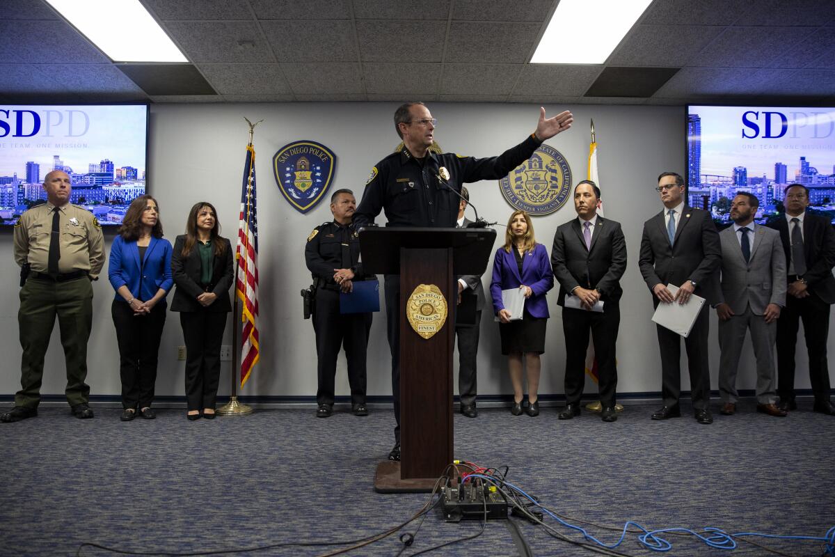 A person in a police uniform raises his left arm behind a lectern.