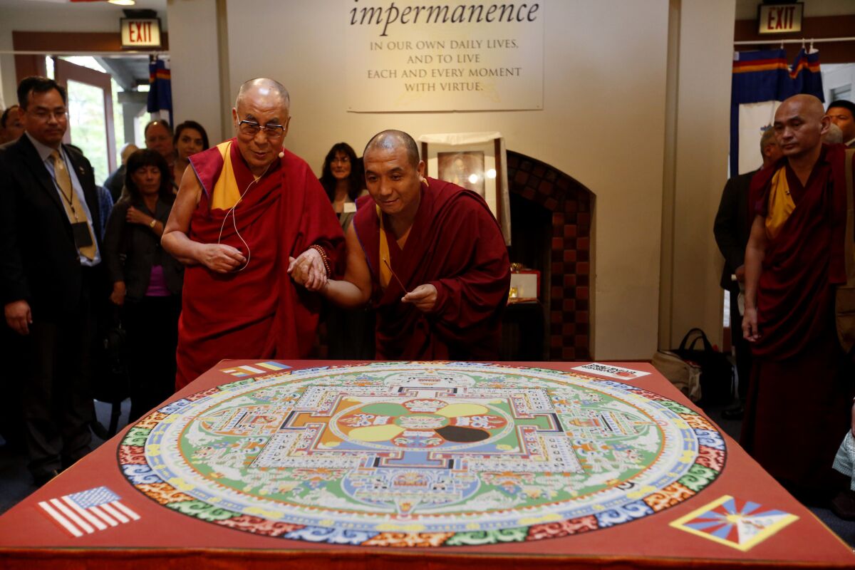 The 14th Dalai Lama, left, with Tibetan monk Sherab Chopel, the principal artist who created the mandala, view it together during a private event in Irvine. The sand mandala was created to commemorate the Dalai Lama's 80th birthday.
