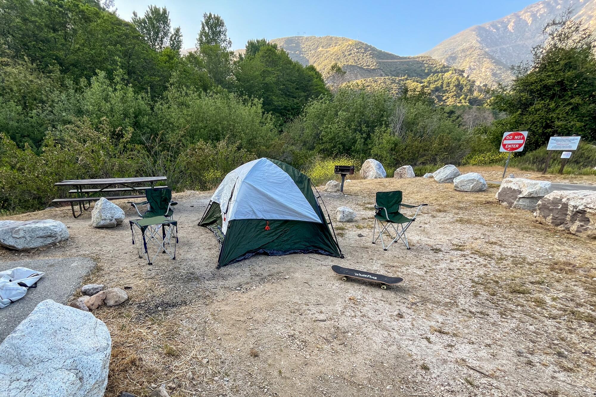 A gray tent set up in the sandy dirt of a campground