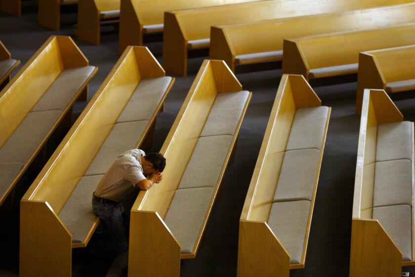 A man prays alone at an Orange County church where five priests were accused of child molestation in 2002.