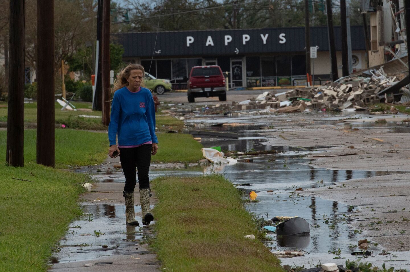 From a sidewalk, a woman observes a debris-filled Lake Charles street.