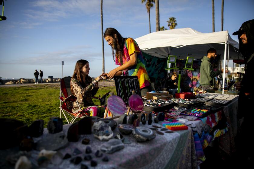 San Diego, CA - December 10: Alexis Keenan and Jay Manypenny, who moved to San Diego from Cleveland, Ohio, with a trove of their friends' art to sell, run a street vendor stand selling crystals and handmade jewelry on the oceanfront in the Ocean Beach neighborhood on Friday, Dec. 10, 2021 in San Diego, CA. (Sam Hodgson / The San Diego Union-Tribune)