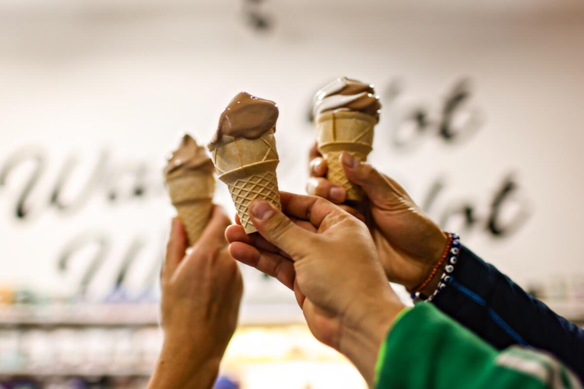 Three hands lift ice cream cones up in a toast