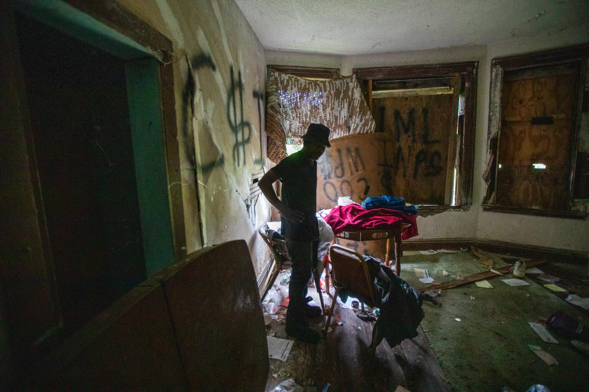Jimmie Mac Lee stands in a room with boarded up windows, graffiti and debris.